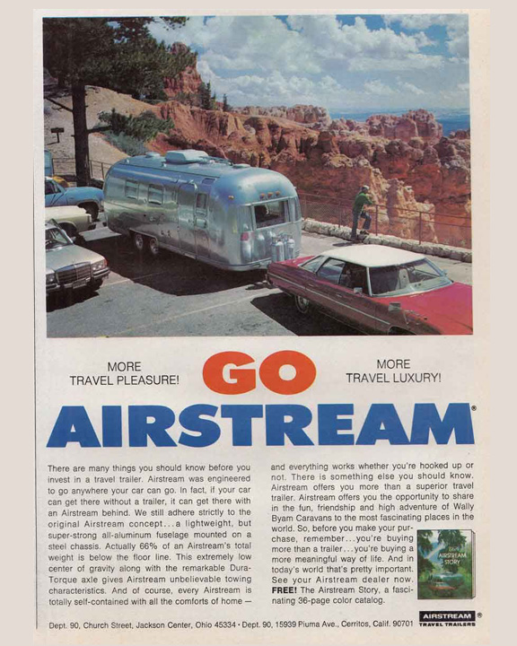 Silver Airstream travel trailer parked in a lot by a canyon overlook with cars nearby, promoting travel with AIRSTREAM GO visually.