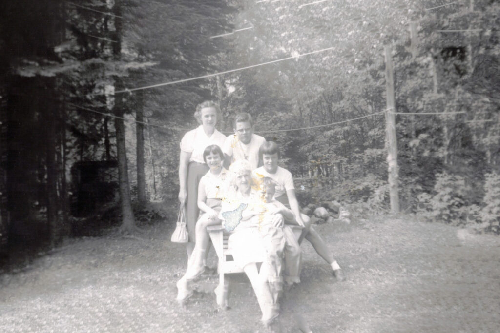 Group of adults posing together in a garden, some seated on a chair, smiling at the camera.