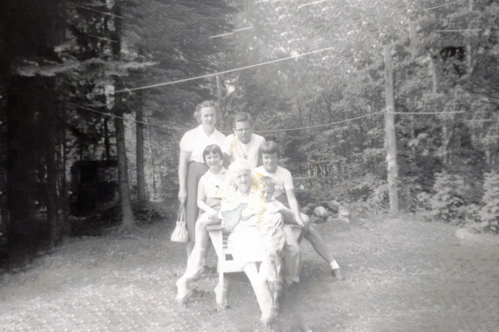 Group of adults posing together in a garden, some seated on a chair, smiling at the camera.