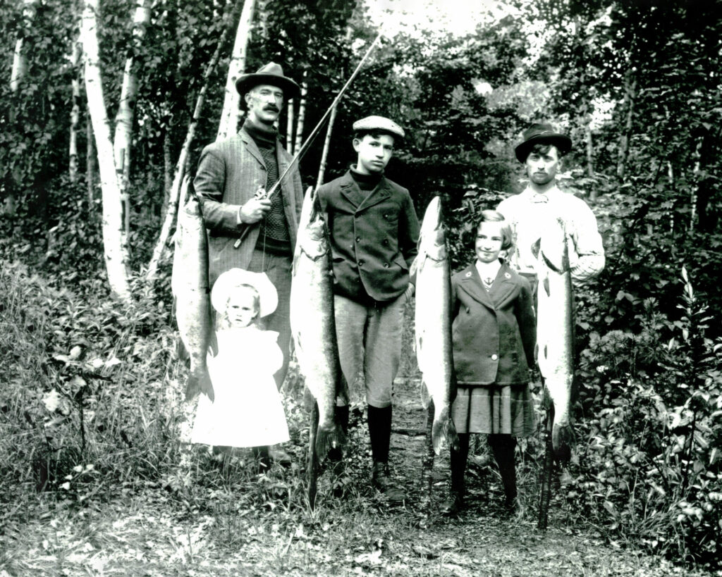 Family posing in a wooded area with several large fish displayed after a fishing trip.