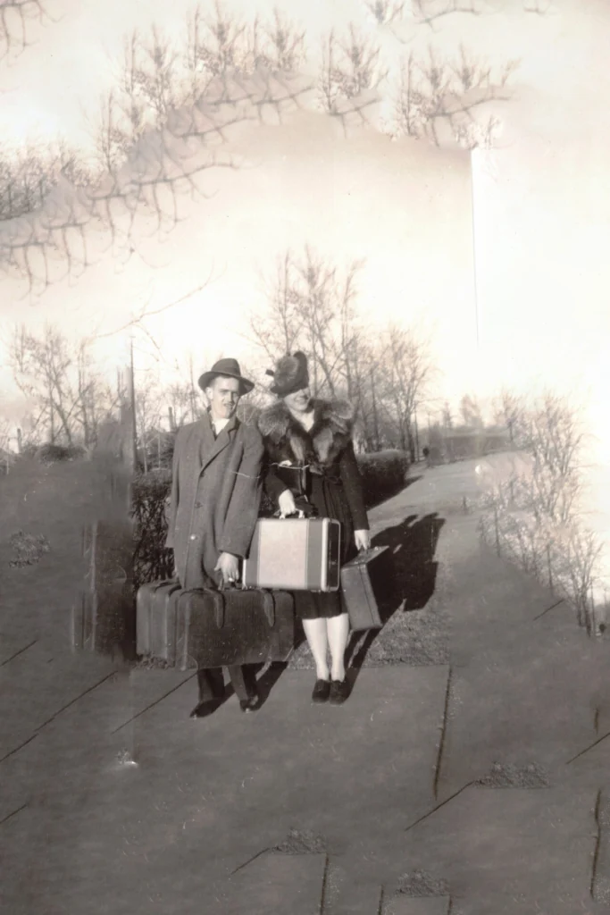 Couple in vintage clothing with multiple suitcases on a sidewalk in a black-and-white photo.