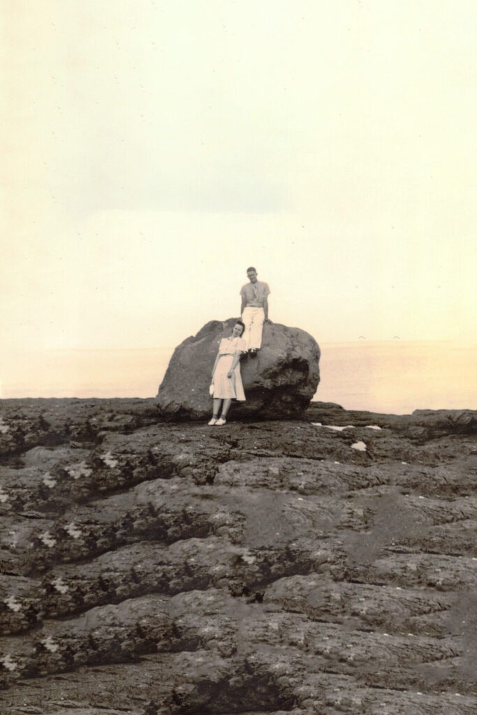 Two people pose on a large rock at a rocky shore, with the sea in the background (vintage photo).