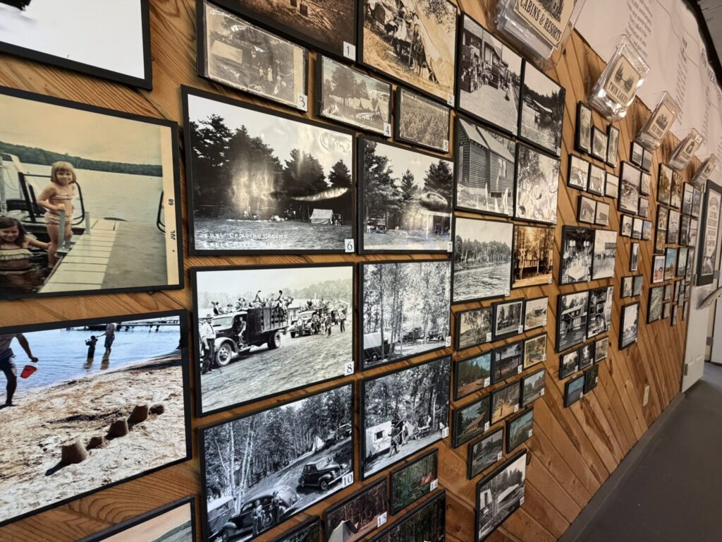 Wall of vintage black-and-white photos and postcards arranged in frames along a wooden wall surface.