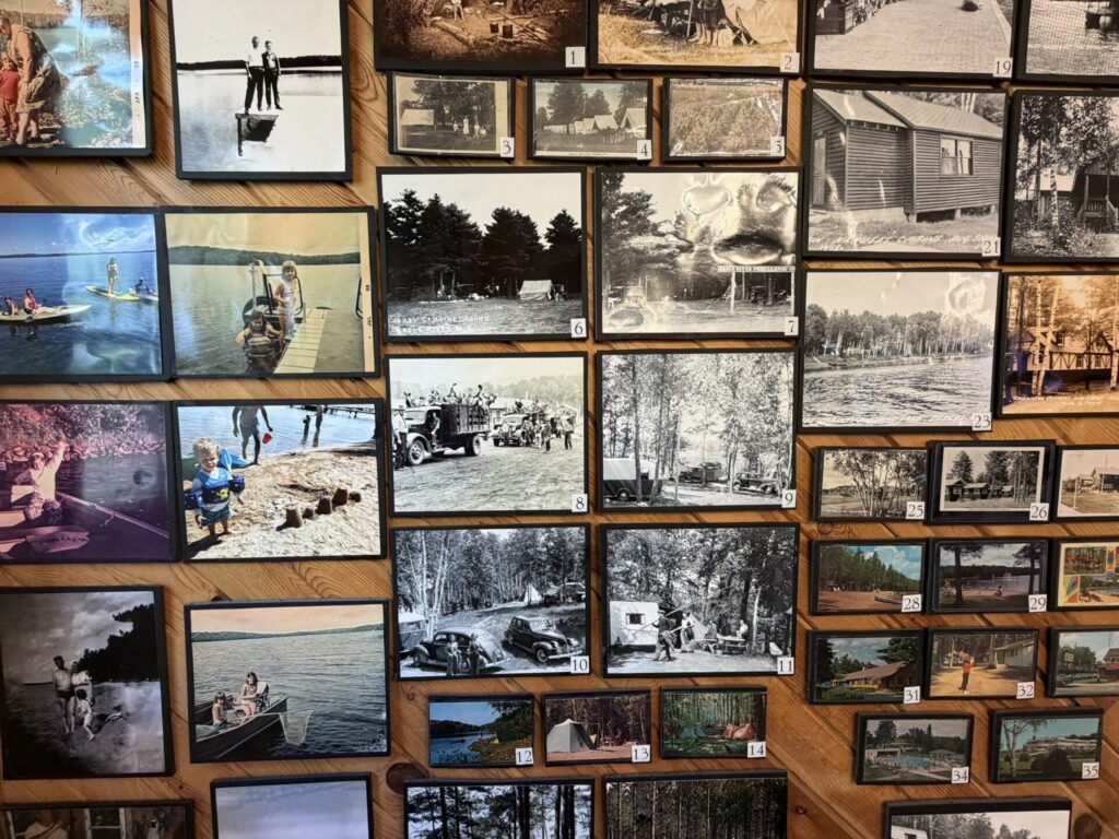 Wall of small framed photos on a wooden wall showing vintage outdoor scenes: lakes, forests, campers, and families in summer settings (collage).
