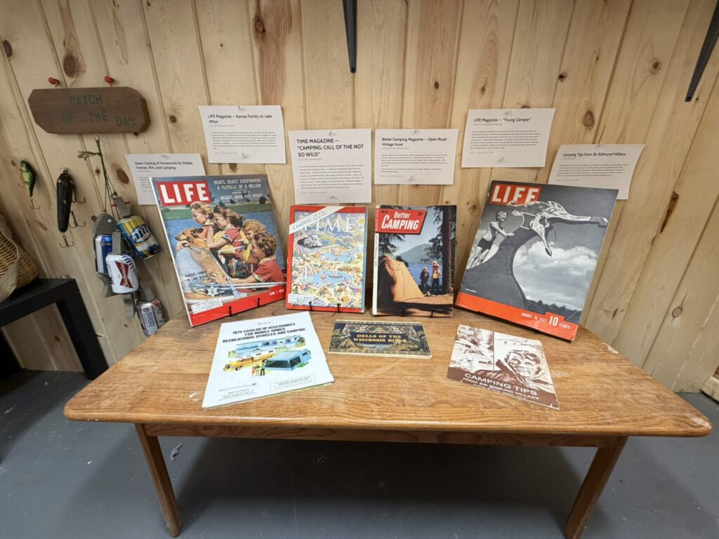 Wooden table with vintage LIFE magazines and camping pamphlets displayed against a wood-paneled wall