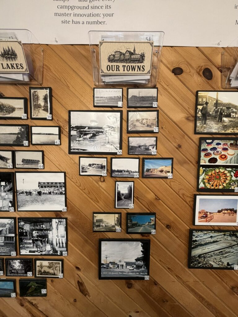 Display of many small black-and-white town photos mounted on a wooden wall, with a central 'Our Towns' card above them.