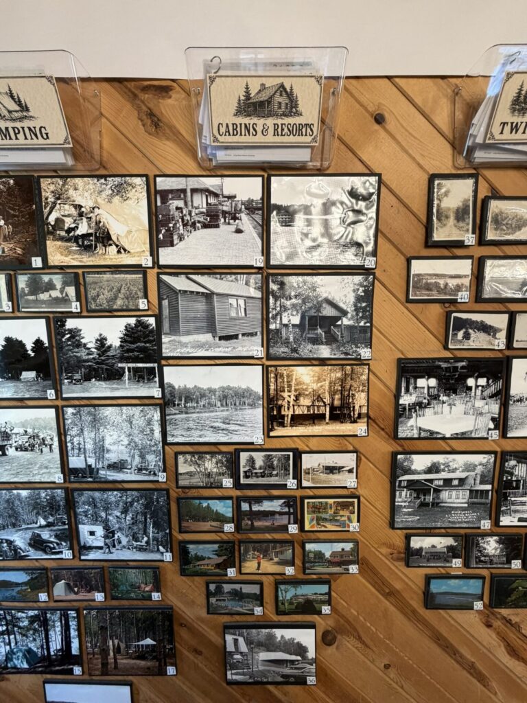 Wall display of numerous small black-and-white photos of cabins, camping, and landscapes on a wooden surface, with a 'Cabins & Resorts' sign above.