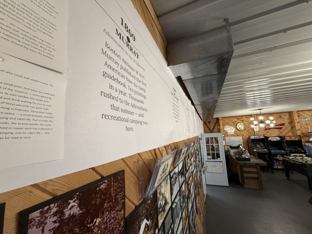 Wall of museum panels with large typography and framed photos on a wood panel wall, ceiling ducts visible.